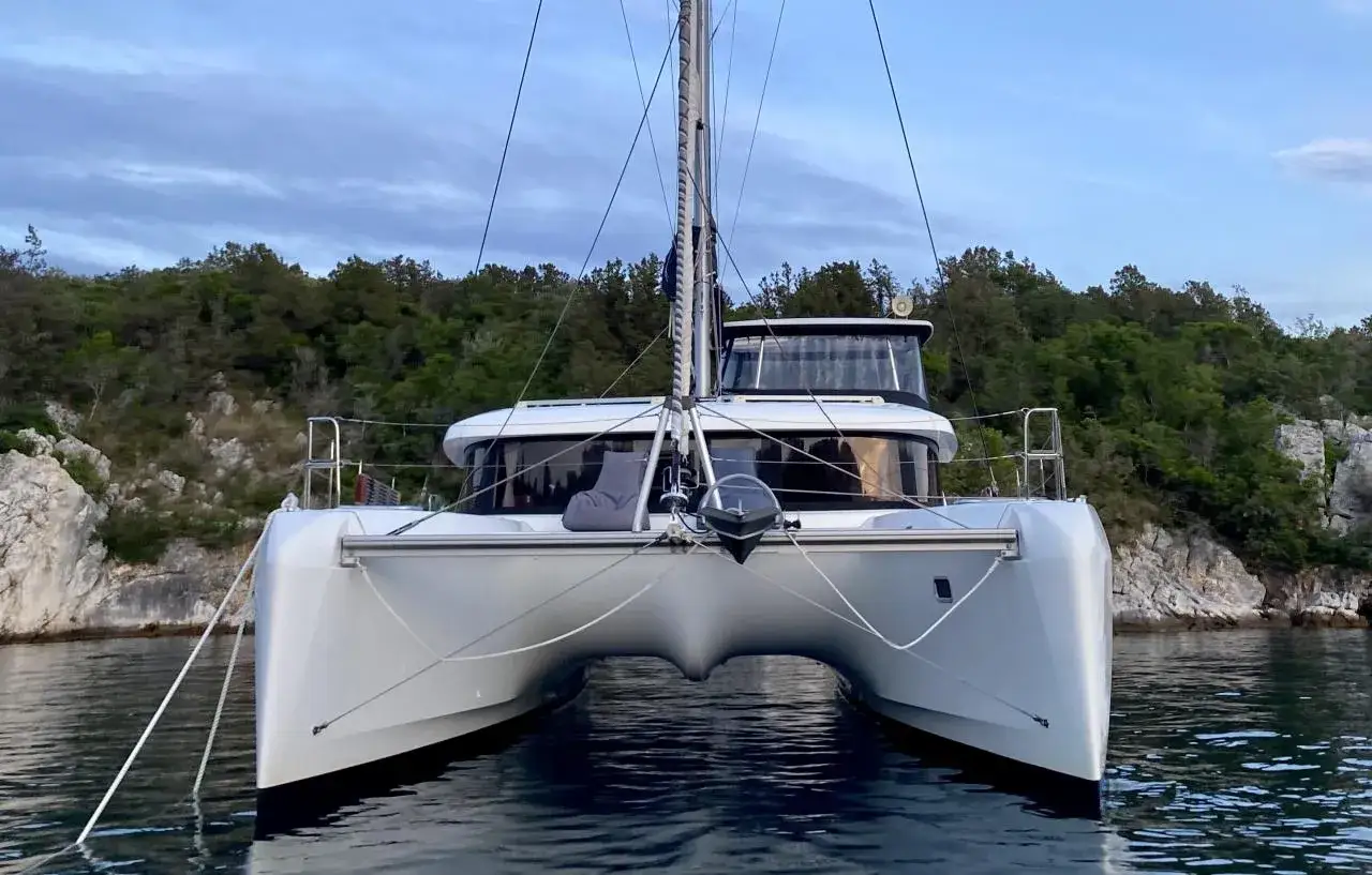 Ein moderner Katamaran mit zwei Rümpfen, der wie ein schwimmendes Haus aussieht, ankert vor einer bewaldeten Küste.