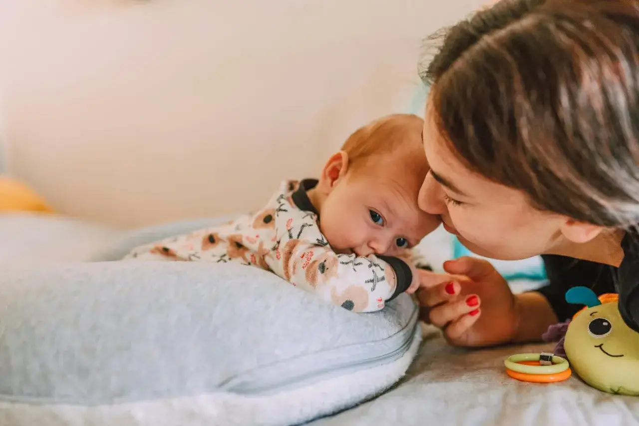 Mama pochyla się nad dzieckiem, które leży na poduszce. Szybki oddech u noworodka może być naturalny, ale czujność rodzica jest ważna.