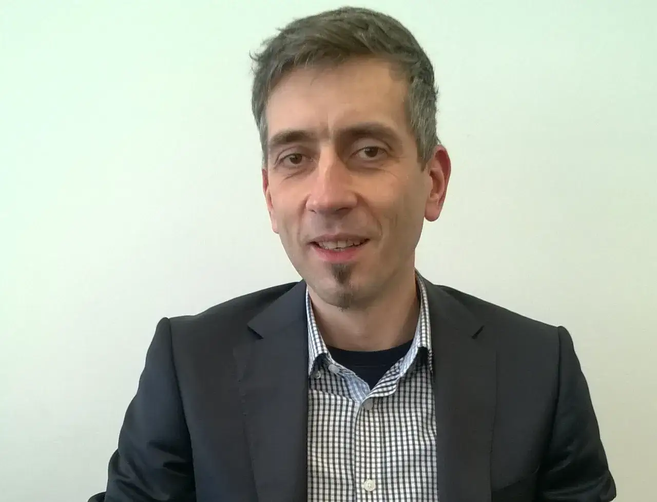 Maciej Kasprzak w czarnym garniturze i koszuli w kratę, z charakterystyczną bródką.