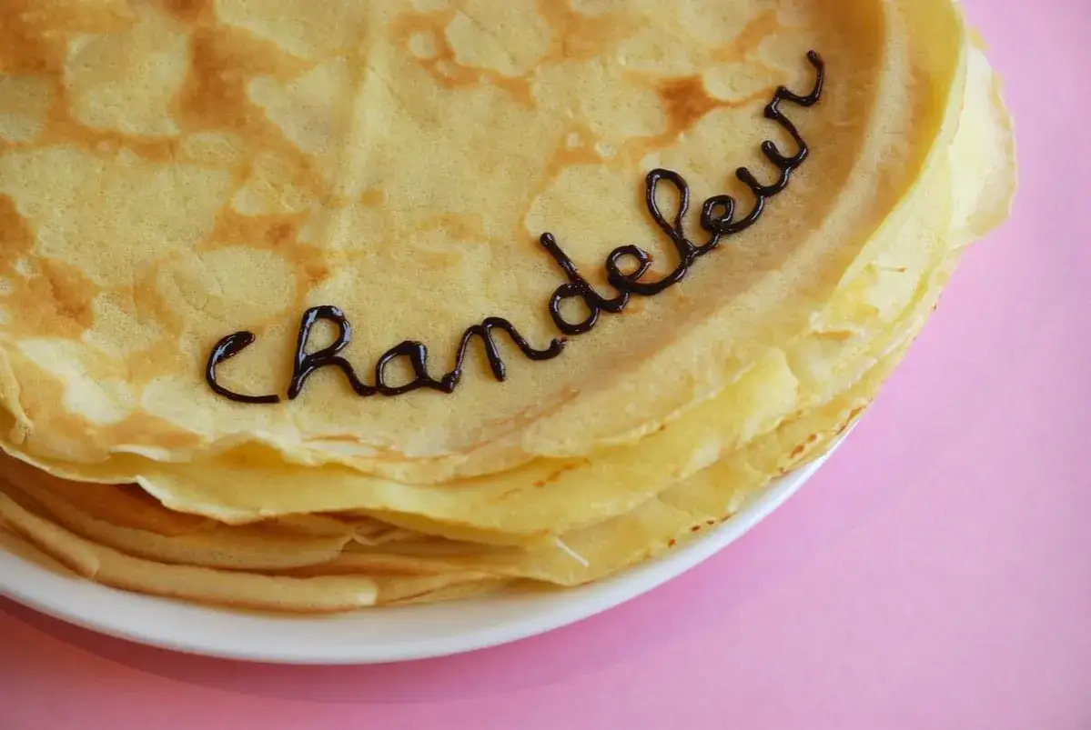 Une pile de crêpes dorées, décorées avec du chocolat formant le mot "Chandeleur". Un délice pour célébrer qu'est-ce que la Chandeleur.