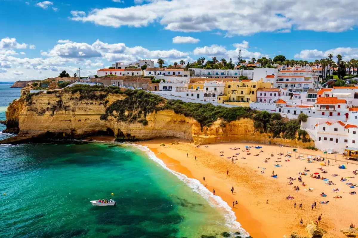 Coastal town with white buildings on cliffs overlooking a sandy beach and turquoise water.