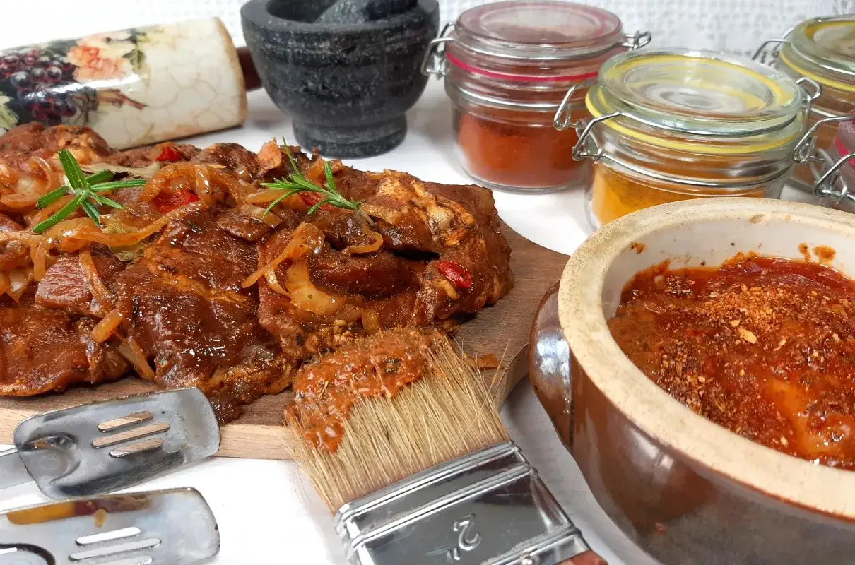 Pyszna marynata do karkówki na grilla, gotowa do użycia. Mięso już w niej pływa, a obok stoją przyprawy.
