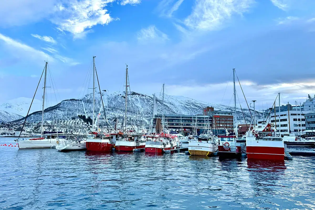 Segelboote und Fischerboote liegen im **Tromsø Hafen** vor schneebedeckten Bergen.