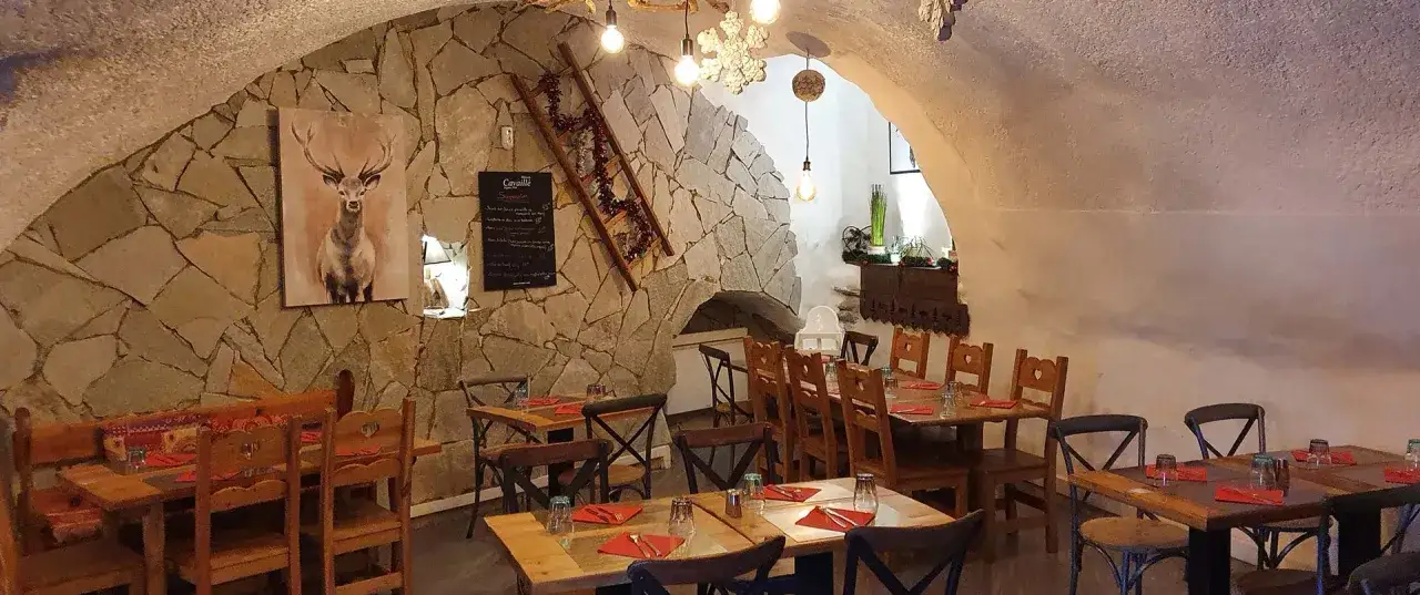 Ambiance chaleureuse dans un des restaurants de Briançon. Murs en pierre, tables en bois, tableau de menu et décoration hivernale.