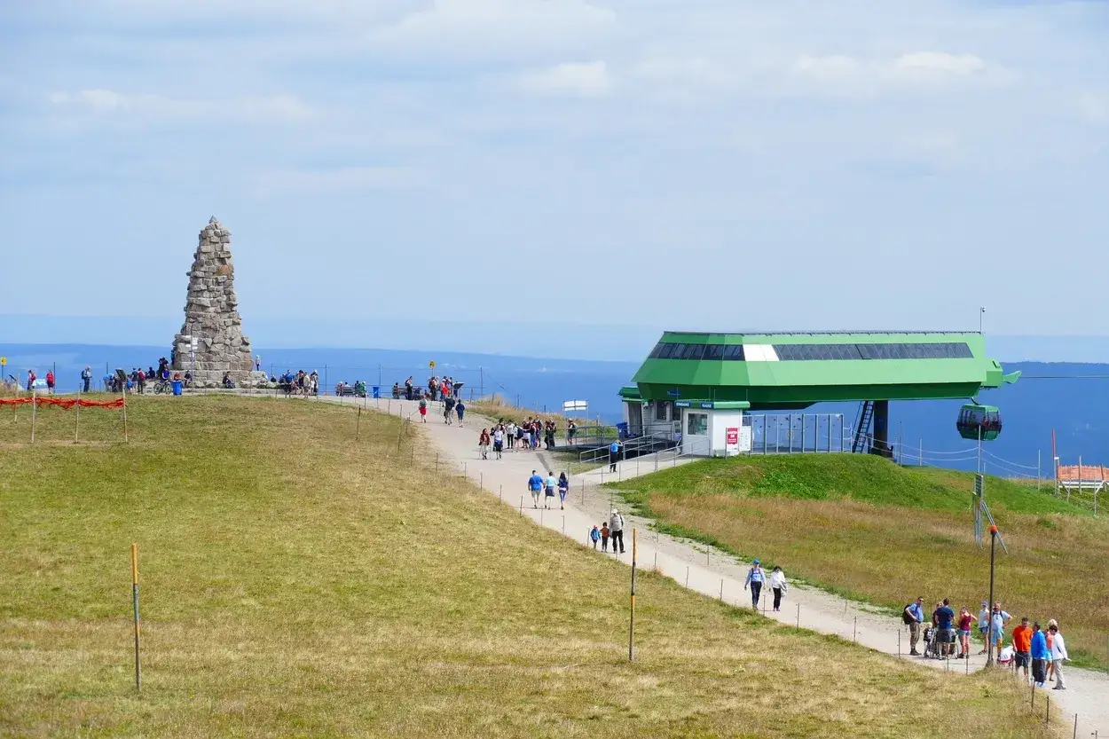 Feldberg: Steinkegel-Denkmal und Seilbahnstation mit Wanderern auf einem grasbewachsenen Hügel.