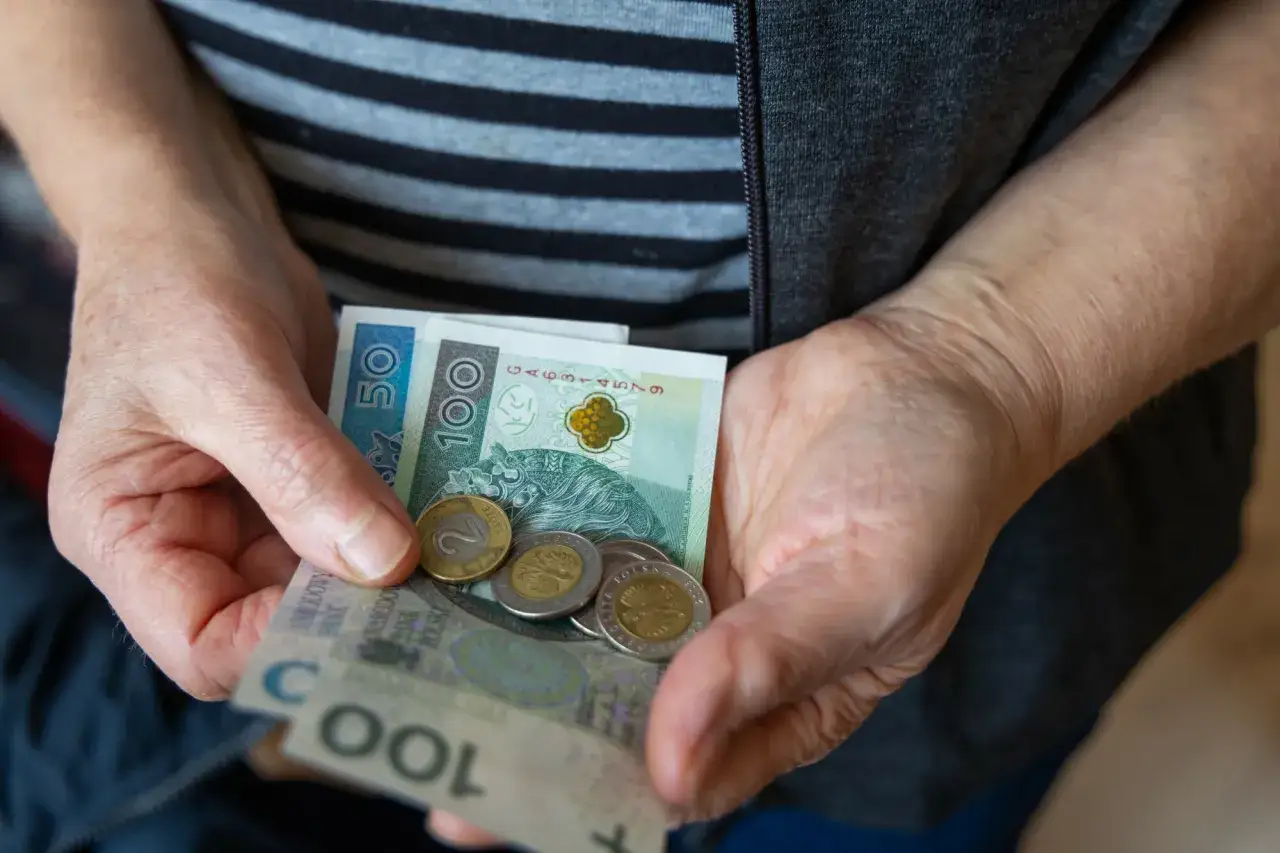 Dłonie starszej osoby trzymają polskie banknoty i monety. To symbol troski o przyszłość i waloryzacja emerytury.