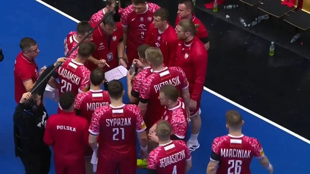 Drużyna piłki ręcznej Polska w czerwonych strojach z białymi detalami, podczas narady taktycznej przed meczem z Niemcami.