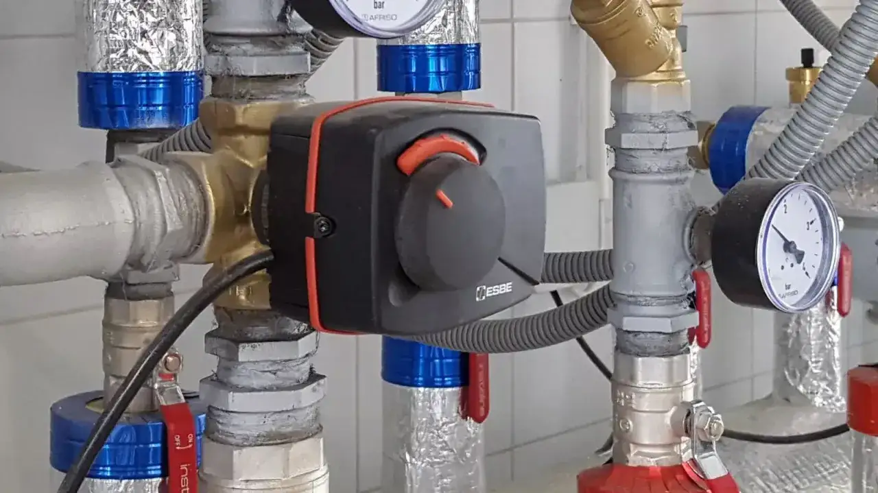 Montaż zaworów wody z termostatycznym regulatorem ESBE. Widoczne manometry i izolowane rury.