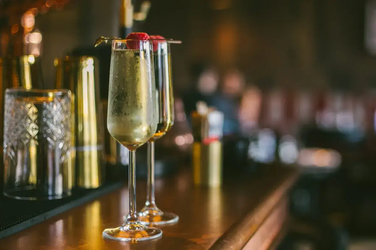 Dwa kieliszki musującego drinku z Prosecco i Cava, ozdobione malinami, stoją na barze obok stylowych akcesoriów.