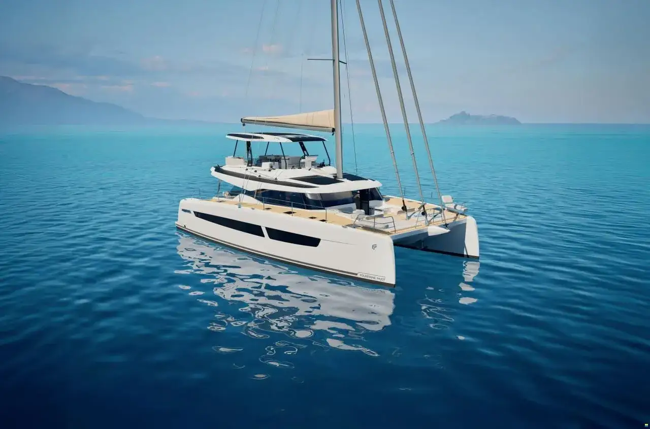 Eine weiße Katamaran-Yacht, eine FOUNTAINE PAJOT, gleitet auf ruhigem, blauem Wasser. Im Hintergrund sind Berge und eine Insel zu sehen.