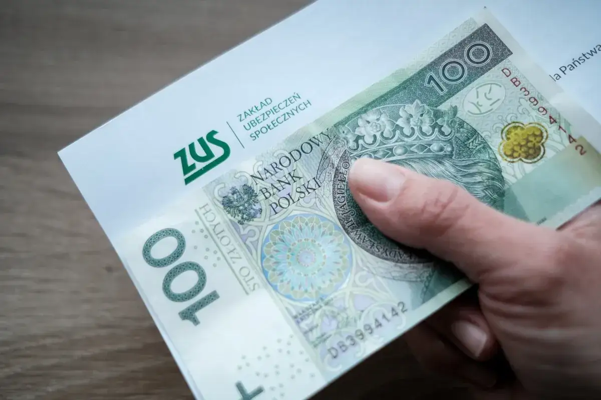 Dłoń trzyma banknot 100 zł i dokument ZUS. Czy na depresję można dostać rentę? Pytanie o świadczenia z ZUS.
