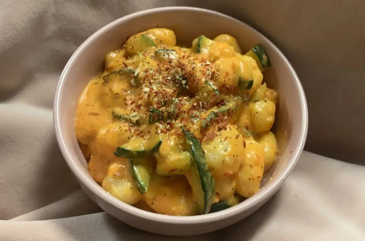 Puszyste gnocchi z cukinią w kremowym sosie, posypane ziołami i płatkami chili. Pyszne gnocchi z pesto w miseczce.