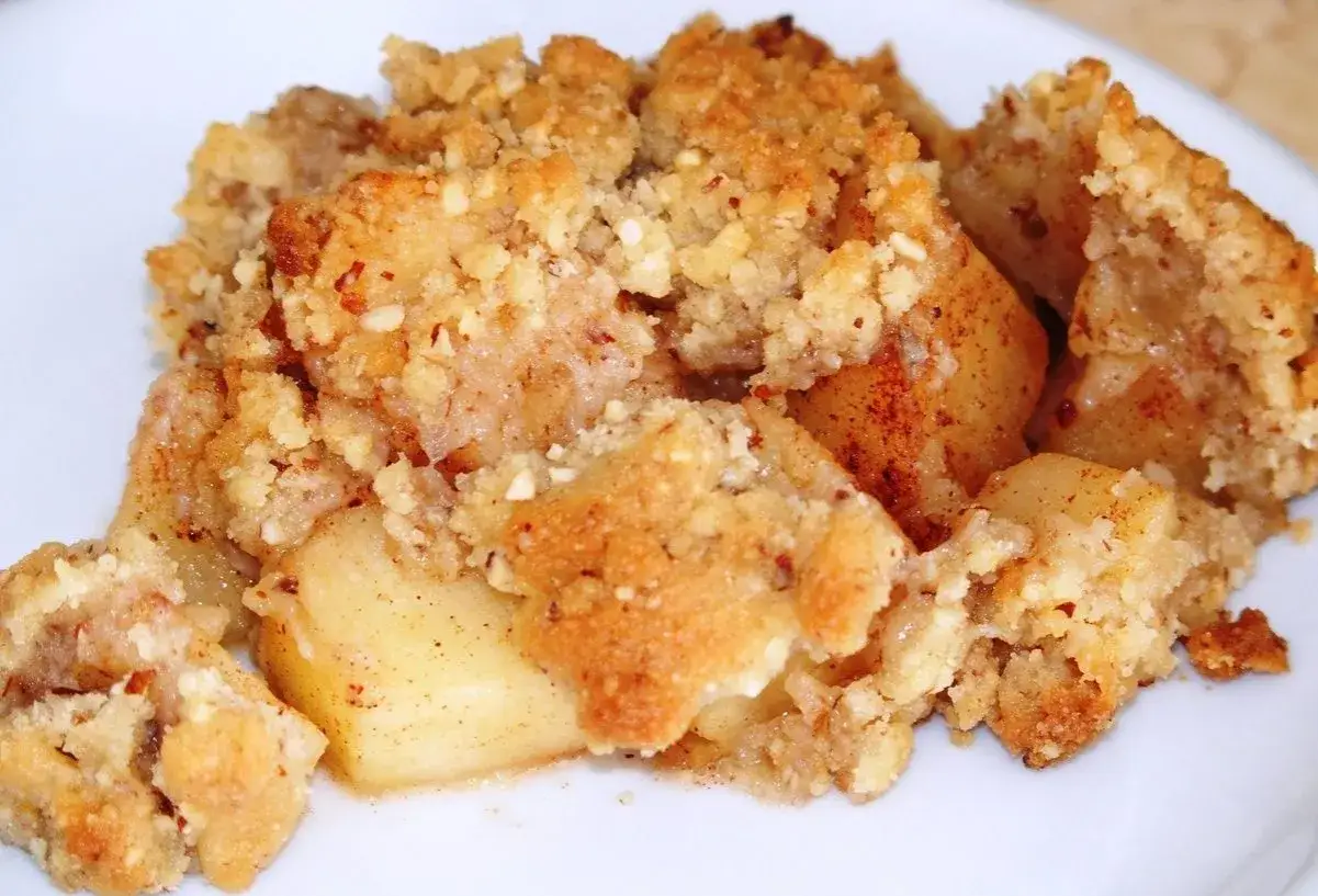 Un délicieux crumble aux pommes à l'ancienne, avec des morceaux de pommes fondantes sous une couche dorée et croustillante de pâte sablée et d'amandes.