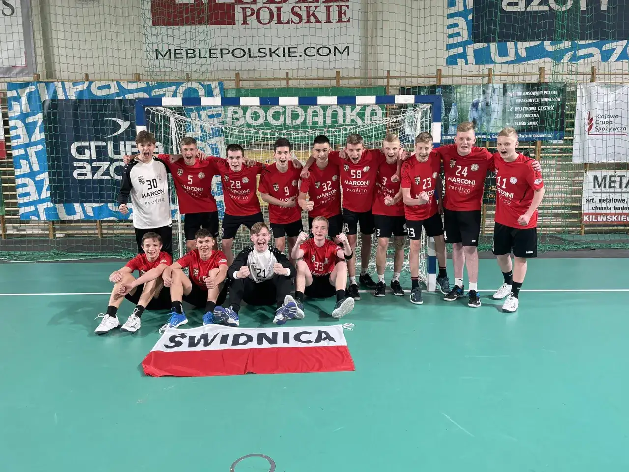 Drużyna piłki ręcznej z numerami na koszulkach, w tym Damian Borkowski, świętuje zwycięstwo.