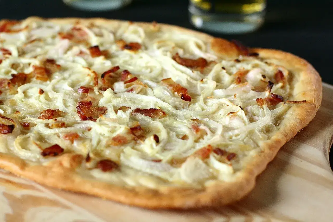 Flammekueche généreuse garnie d'oignons crus ou cuits et de lardons croustillants, prête à être dégustée.