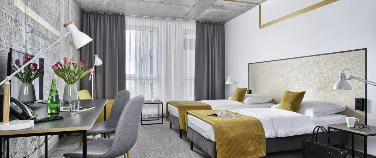 Pokój hotelowy z dwoma łóżkami, biurkiem i kwiatami. Idealne miejsce na wcześniejsze zameldowanie w hotelu.