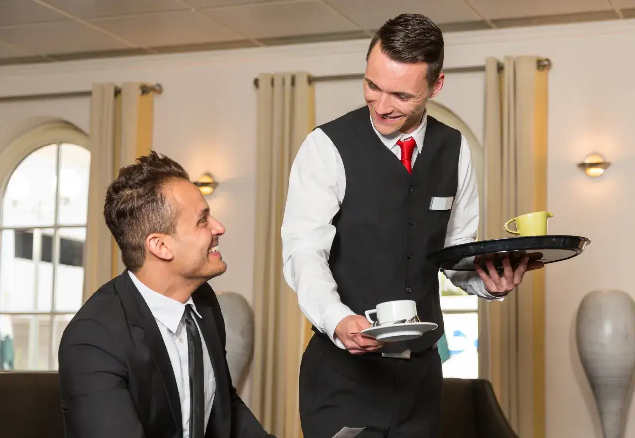 Un serveur souriant présente une tasse de café à un client, illustrant le protocole de service à table.