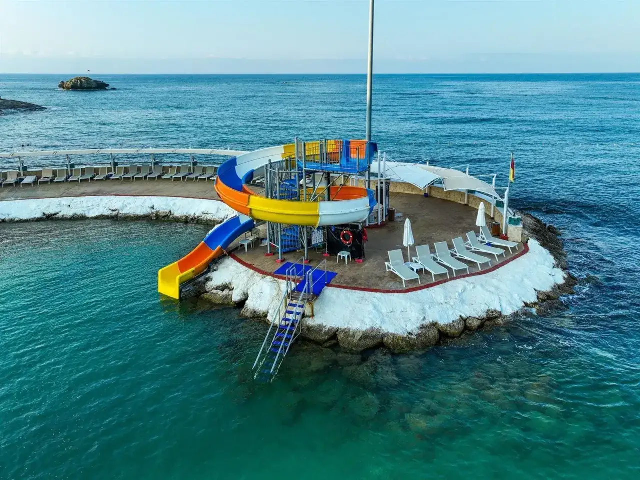 Kolorowe zjeżdżalnie wodne i leżaki na wyspie w Orange County Alanya, nad turkusowym morzem.