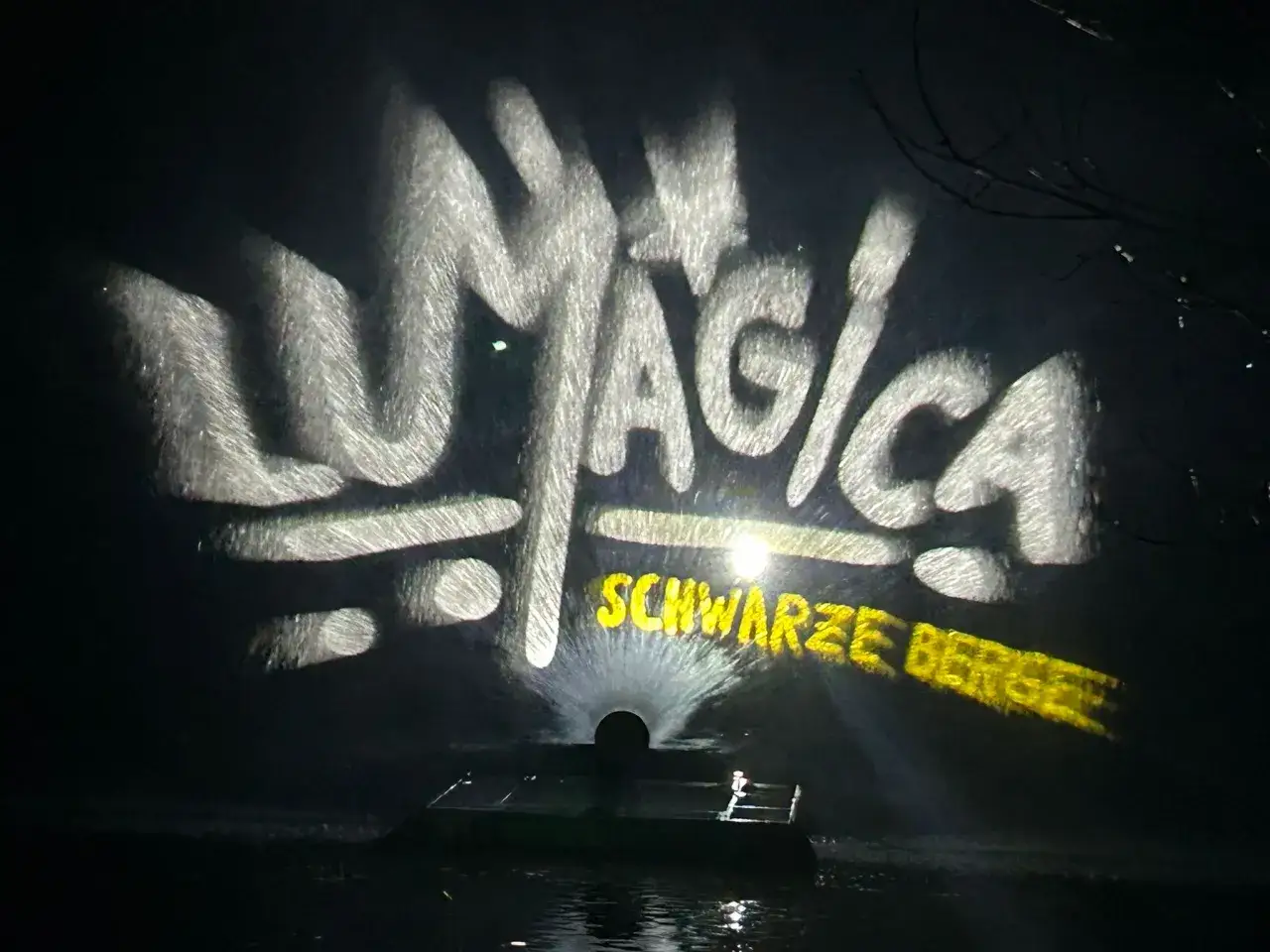 LUMAGICA Schwarze Berge Schriftzug auf Wasserprojektion bei Nacht.