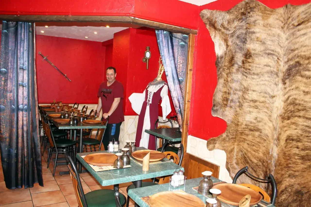 Un homme se tient dans un restaurant moyen âge décoré d'une peau d'ours et d'une épée.