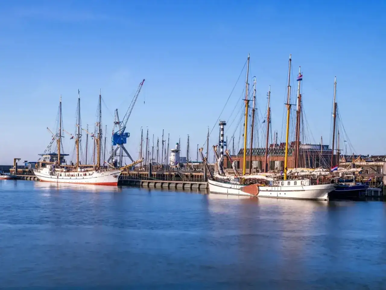 Segelschiffe im Harlingen Hafen, ein Kran ragt in den blauen Himmel.