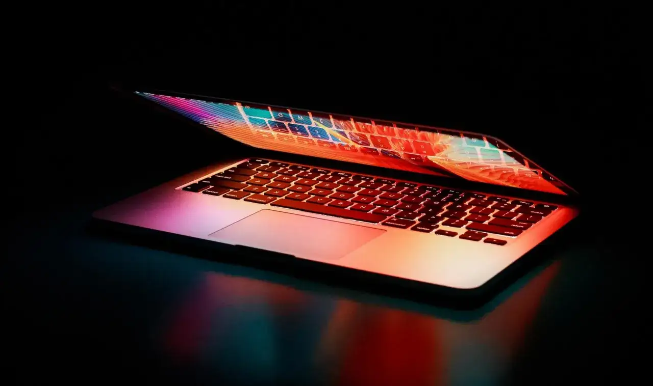 Otwarty laptop z kolorowym podświetleniem klawiatury i ekranu na ciemnym tle.