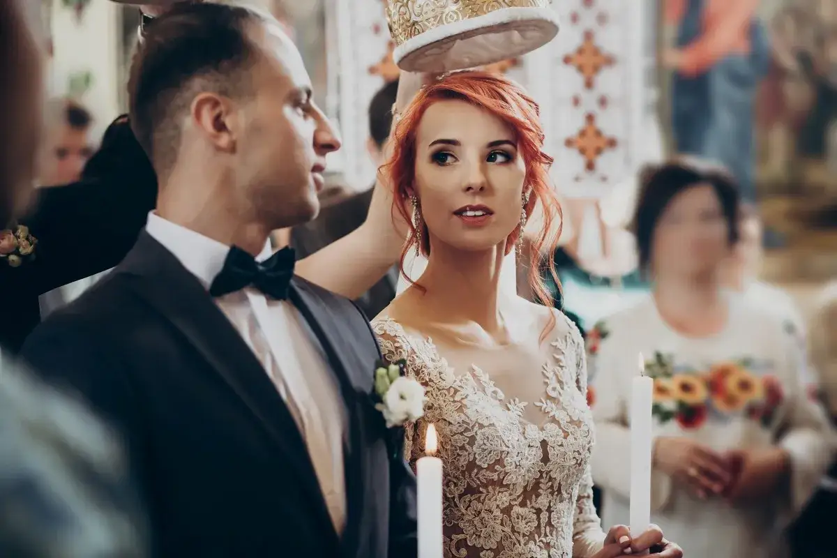 Para młoda podczas ceremonii ślubnej. Panna młoda w koronkowej sukni i pan młody w garniturze, trzymają świece.