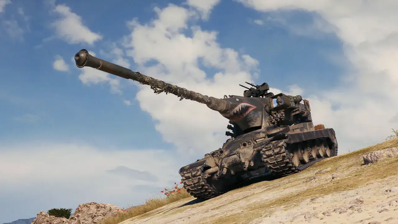 Czołg z malowaniem rekina, jak z modów do World of Tanks, wspina się po piaszczystym wzgórzu pod błękitnym niebem.