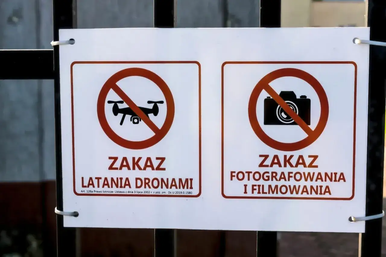 Dwa znaki na płocie: zakaz latania dronami i zakaz fotografowania i filmowania.