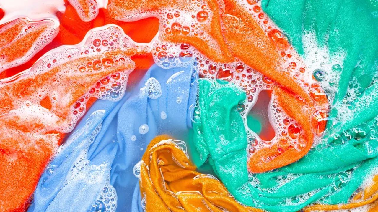 Ropa de color lavadora con burbujas de jabón. Prendas naranjas, azules, verdes y amarillas sumergidas en agua.