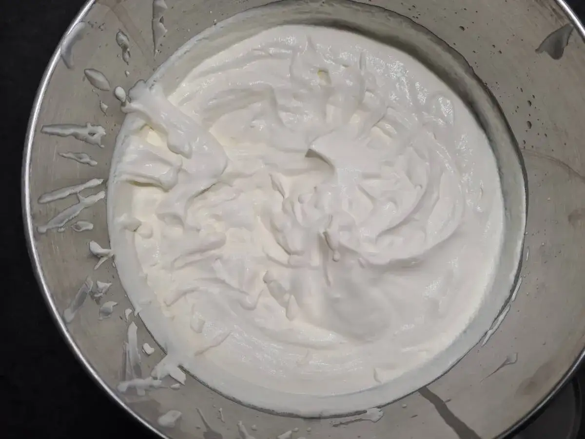 Crème fouettée onctueuse dans un bol en métal, prête à garnir un délicieux gâteau.
