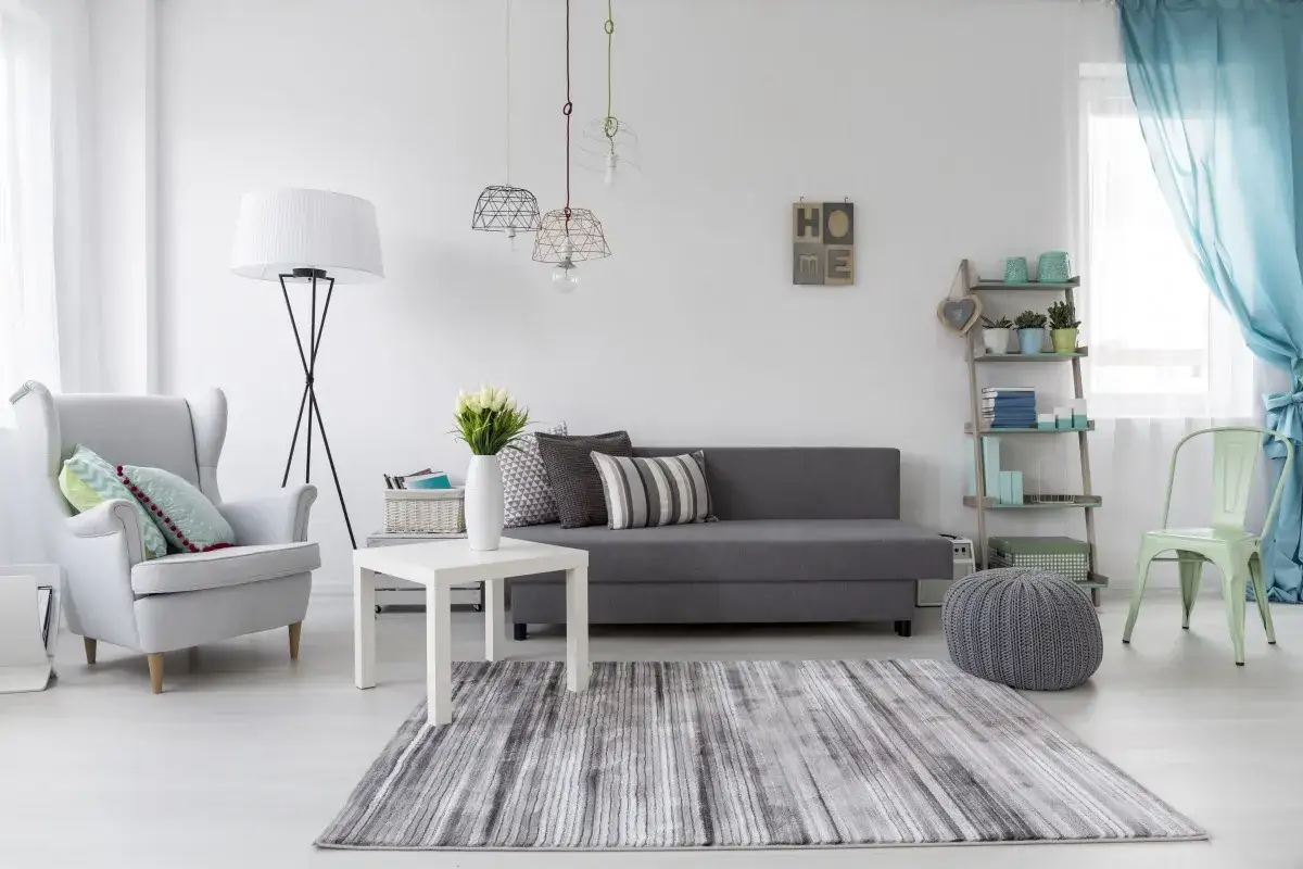 Jasny salon z szarą kanapą i fotelem. Inspiracja, jak pomalować ściany w salonie, by uzyskać taki efekt.