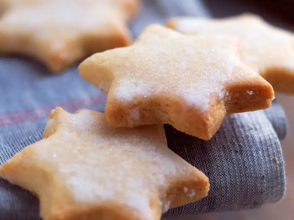 Des sablés au citron en forme d'étoiles, saupoudrés de sucre, reposent sur un tissu bleu.