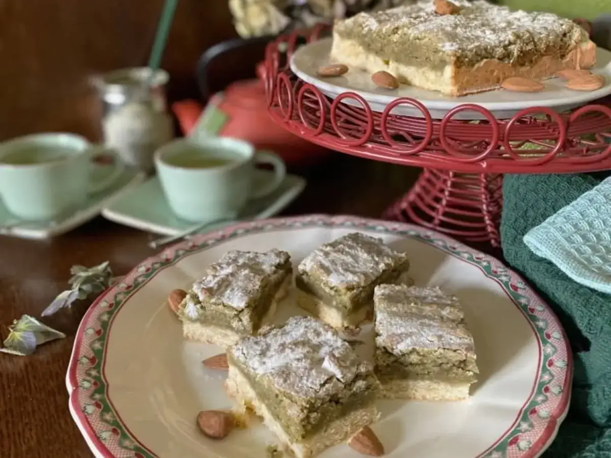 Carrés de croute à thé aux amandes, saupoudrés de sucre glace, servis avec des tasses de thé vert.