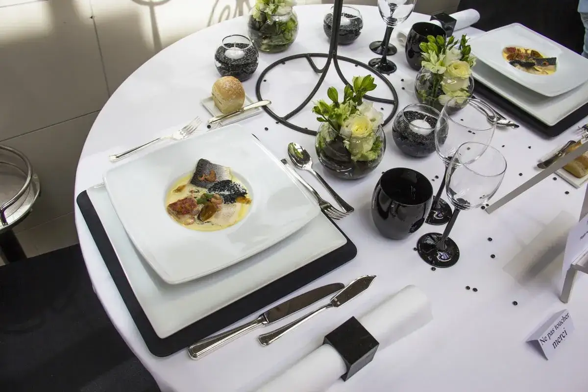 Une table de restaurant dressée avec élégance, un plat de poisson en vedette, des verres noirs et des fleurs.