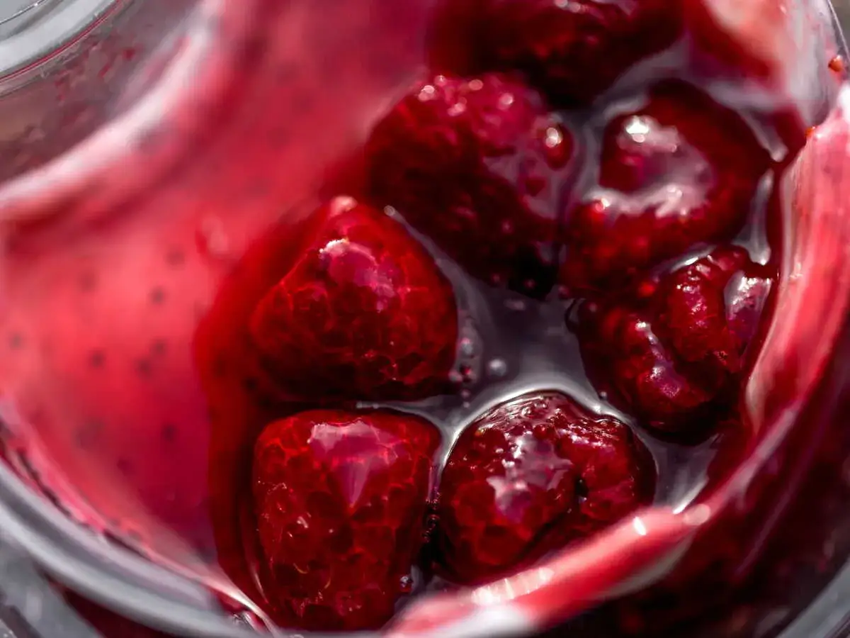 Gros plan sur des framboises dans un liquide rouge vif, parfait pour un nappage framboise facile et gourmand.