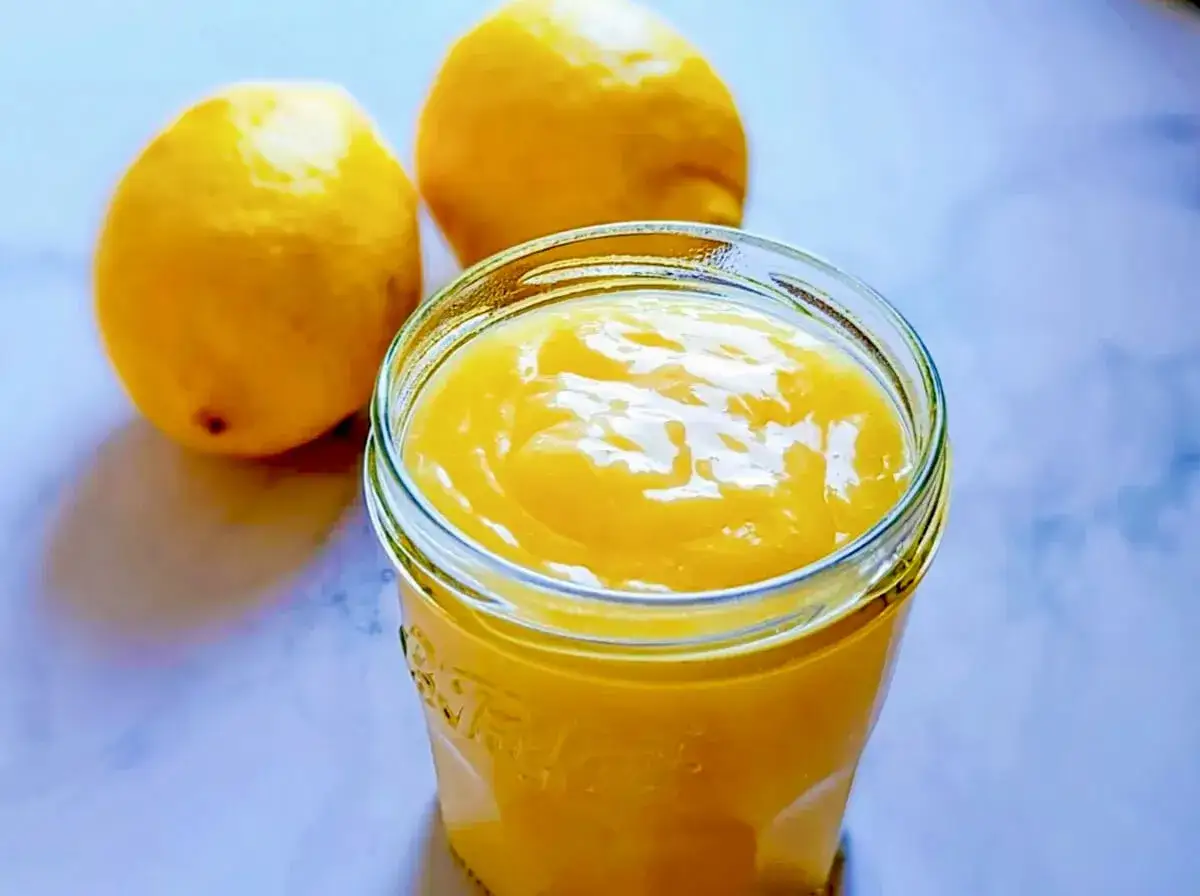 Un pot de lemon curd sans maïzena, onctueux et doré, à côté de deux citrons frais. Parfait pour une touche acidulée.