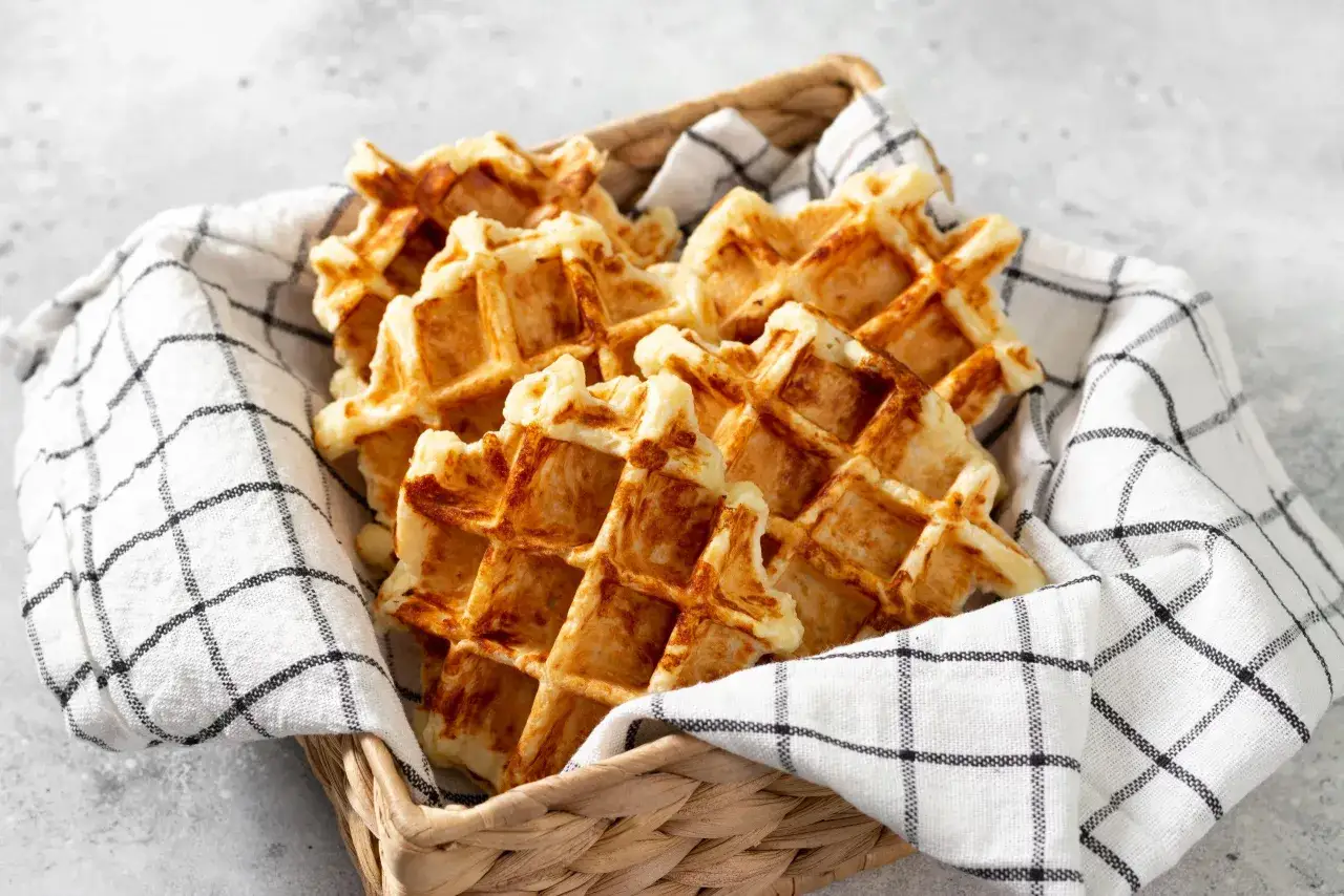 Un panier rempli de gaufres dorées, parfaites pour une recette gaufre rapide. Elles sont présentées sur une serviette à carreaux noirs et blancs.