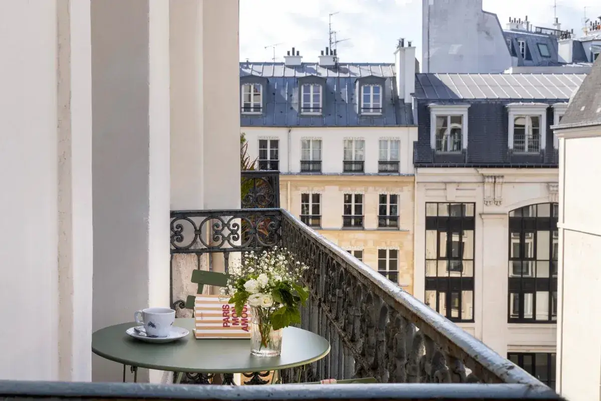 Petit-déjeuner sur le balcon avec vue sur les toits de Paris. Une tasse de café, un livre "Paris mon amour" et des fleurs, un moment de détente au saint-grégoire.