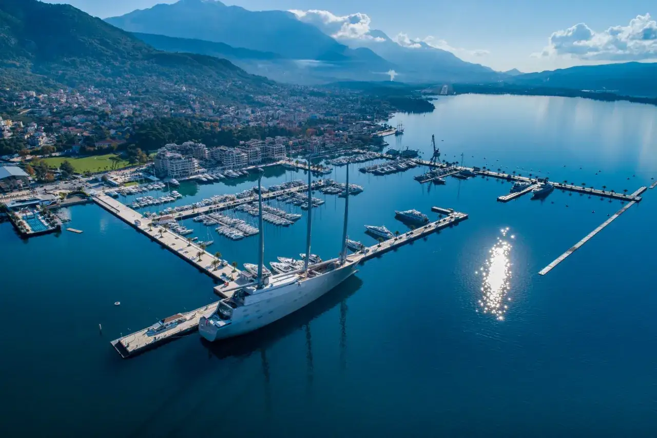 Ein riesiges Segelschiff liegt im porto hafen, umgeben von vielen Yachten und einer Stadt am Fuße von Bergen.