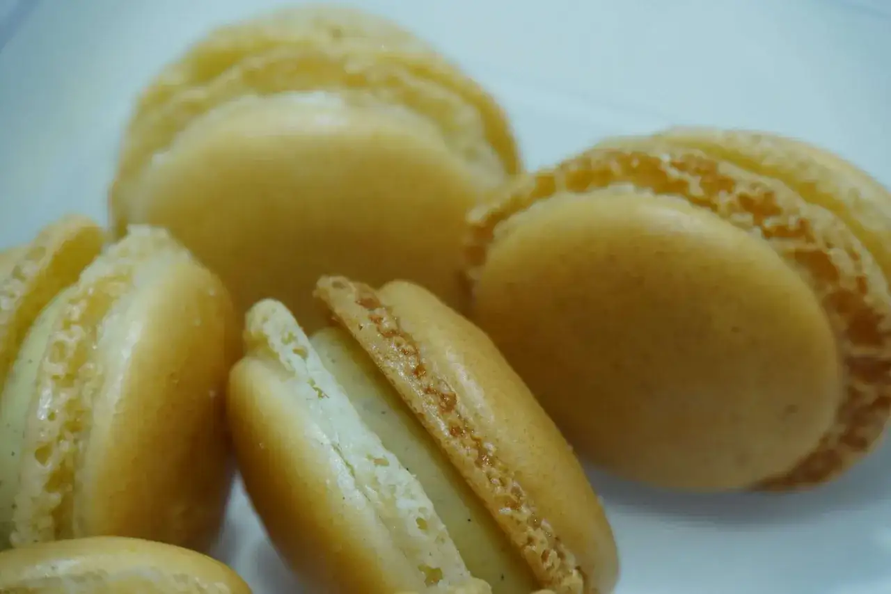 Macarons dorés à la ganache vanille, leurs coques délicates révèlent une garniture crémeuse et parfumée.