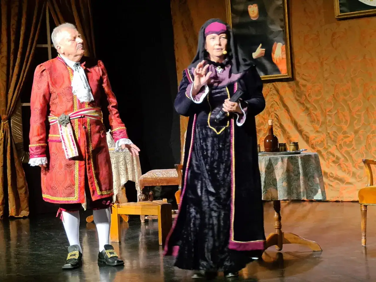 Dwoje aktorów w strojach historycznych na scenie teatralnej.