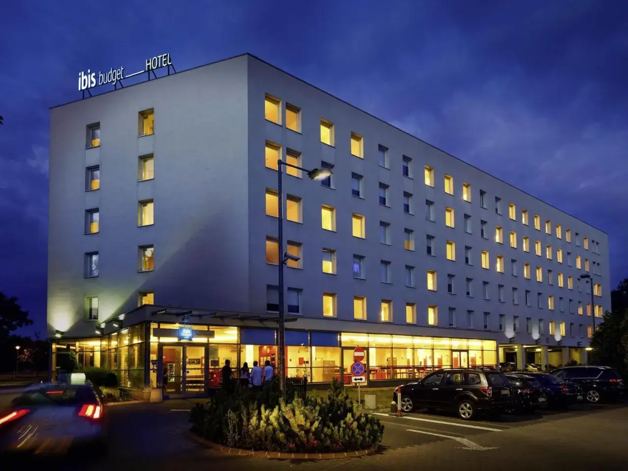 Ibis Budget Warszawa Centrum nocą. Hotel z podświetlanym logo, oknami i parkingiem.