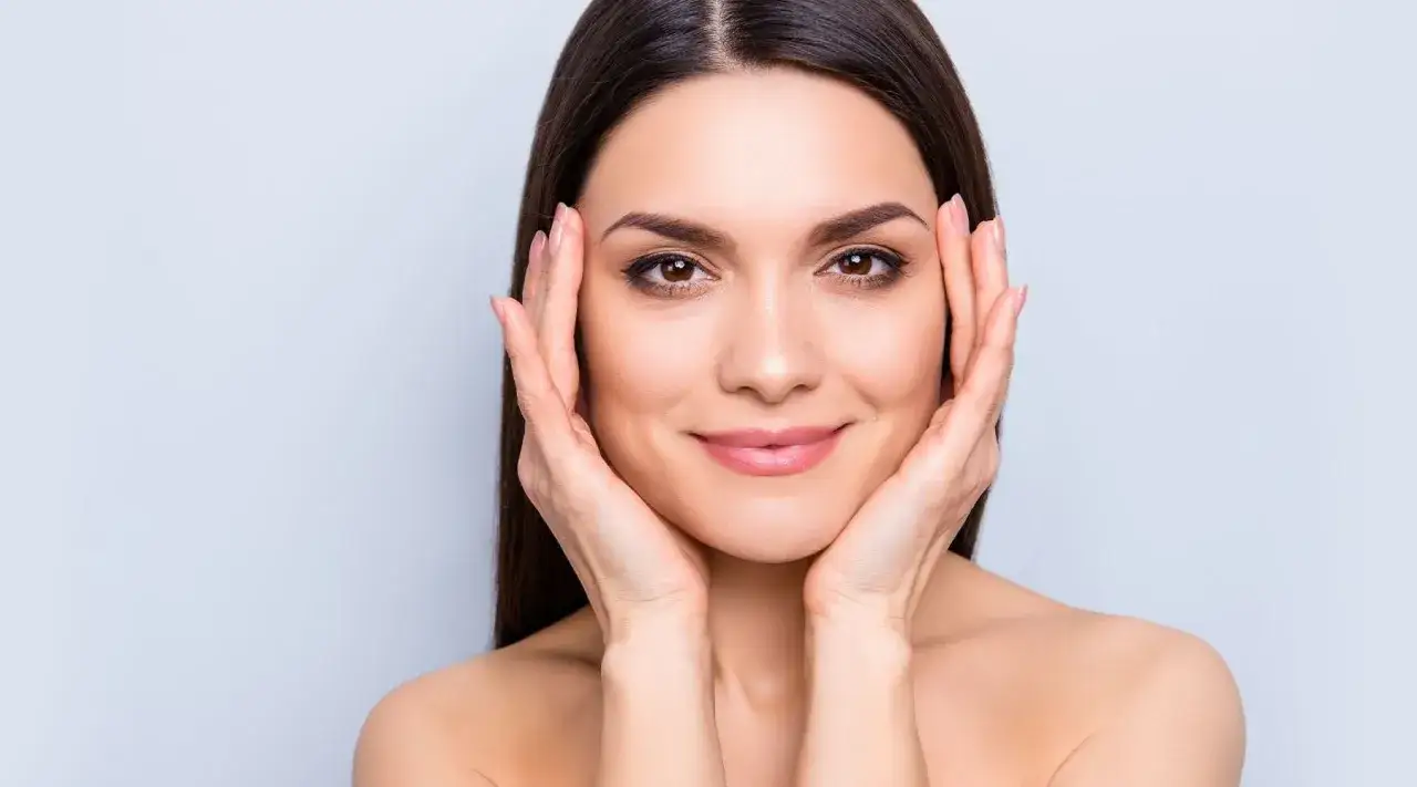 Mujer con piel radiante, resultado del colágeno para la piel. Sus manos acarician su rostro, mostrando una tez suave y luminosa.