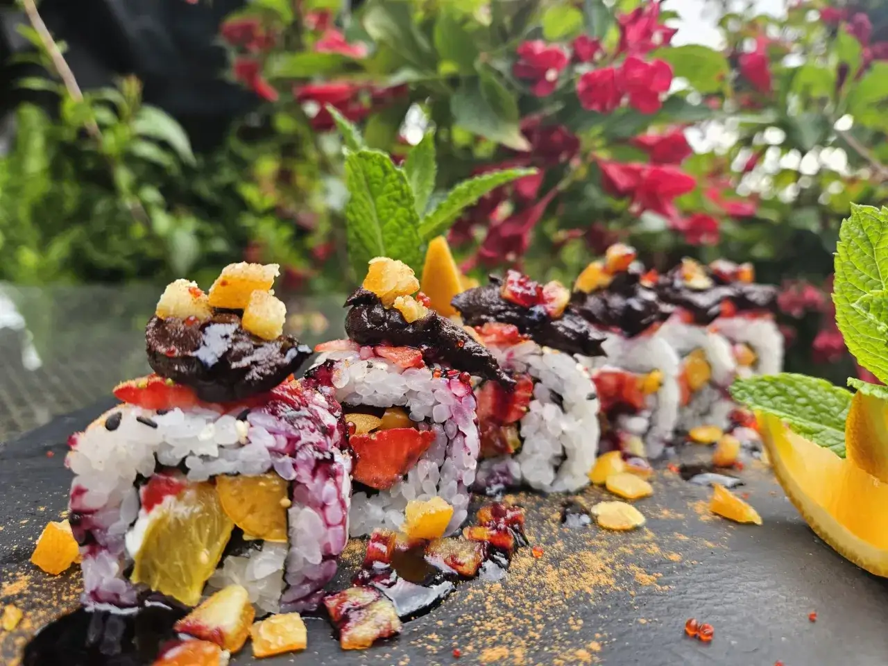 Roladki sushi z owocami, posypane cukrem pudrem i udekorowane miętą i pomarańczą.