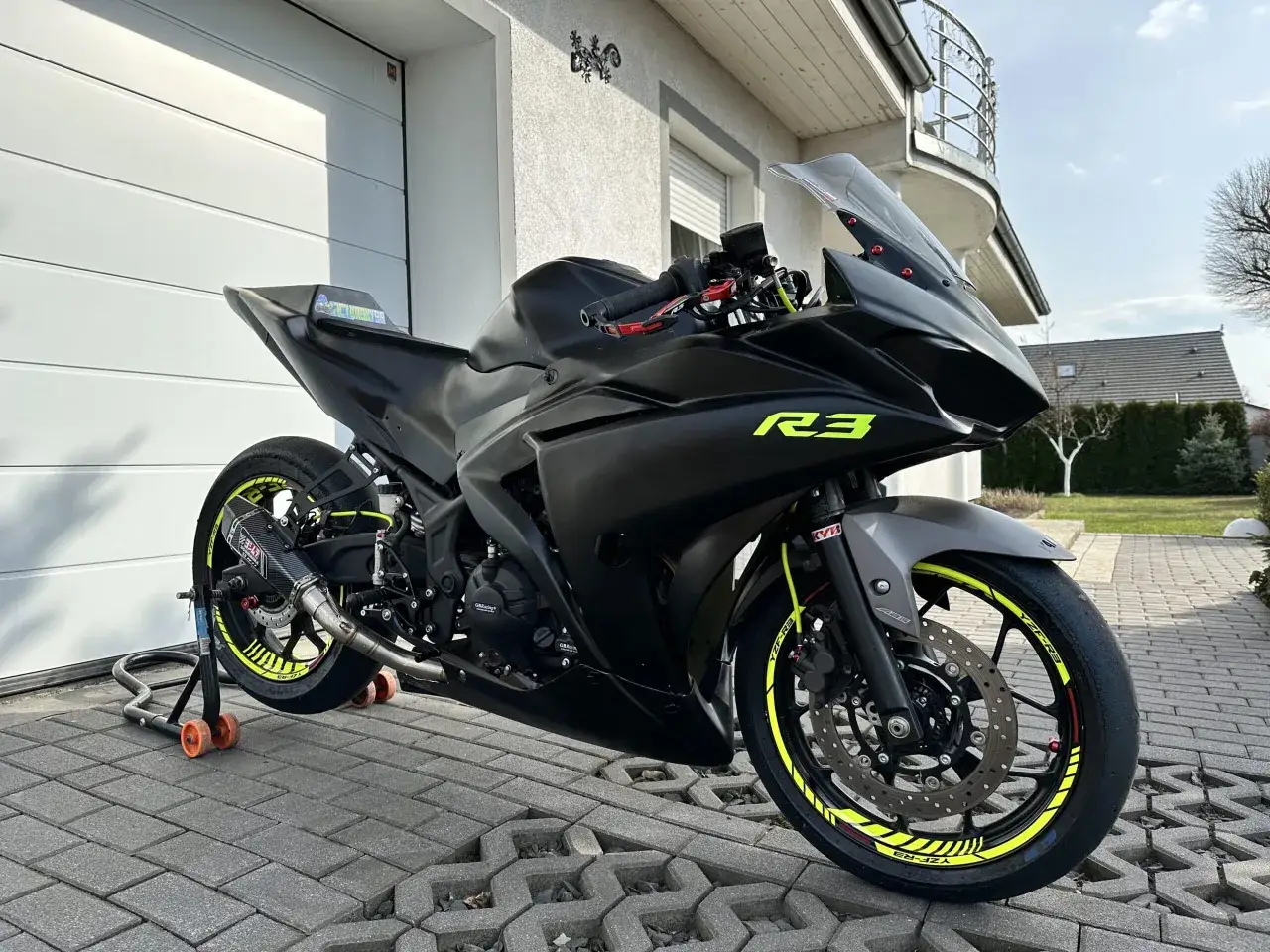 Czarny motocykl Yamaha R3 z żółtymi akcentami na felgach i owiewkach. Widać sportowy wydech Yoshimura. Idealny do poznania yamaha r3 dane techniczne.