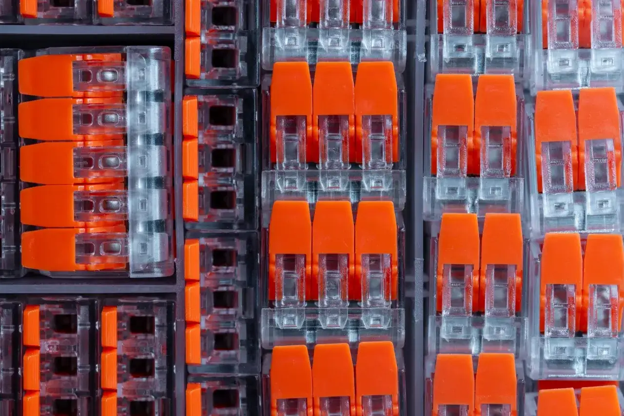 Zbliżenie na pomarańczowe złącza elektryczne w przezroczystych obudowach, ułożone w rzędy.