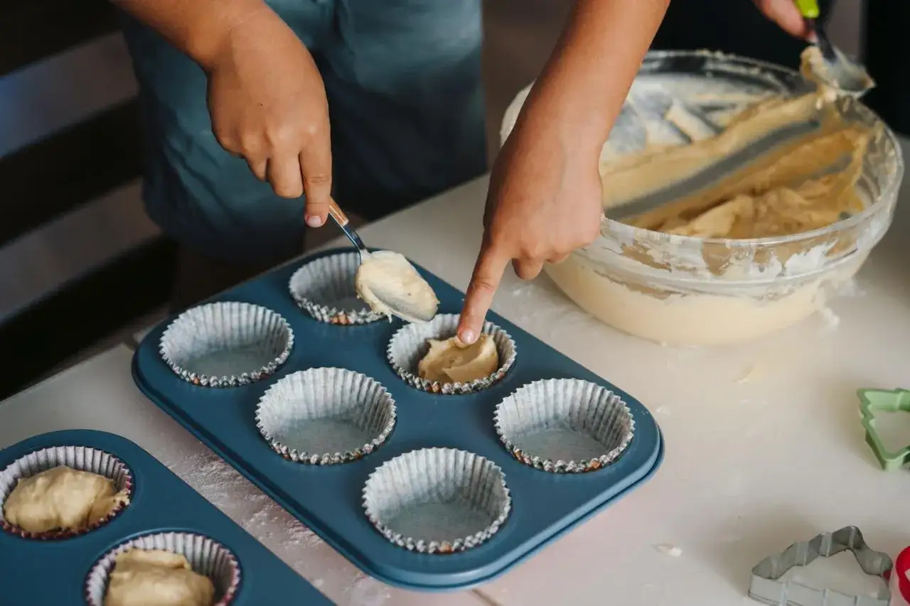 Dziecko nakłada ciasto na muffinki łyżką do formy.