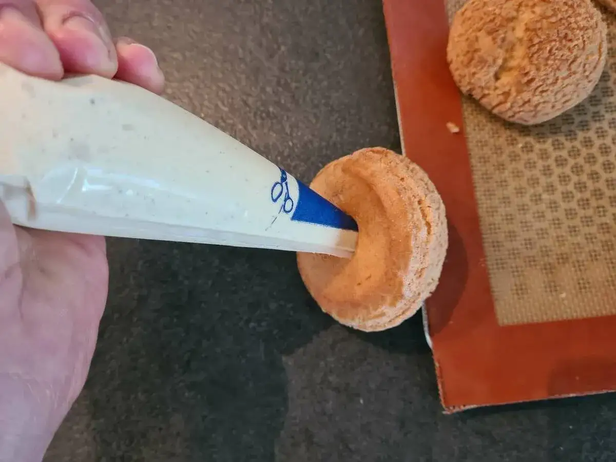 Garnissage d'une pâte à choux profiterole avec une crème onctueuse à l'aide d'une poche à douille.