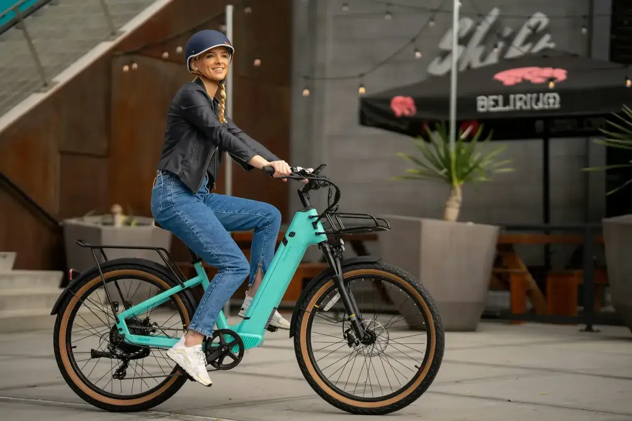 Uśmiechnięta kobieta na turkusowym rowerze elektrycznym. Idealny sposób na skorzystanie z dofinansowania do zakupu roweru elektrycznego i odkrywanie miasta.